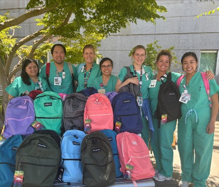 Pain clinic team members wearing scrubs, holding up the backpacks they donated